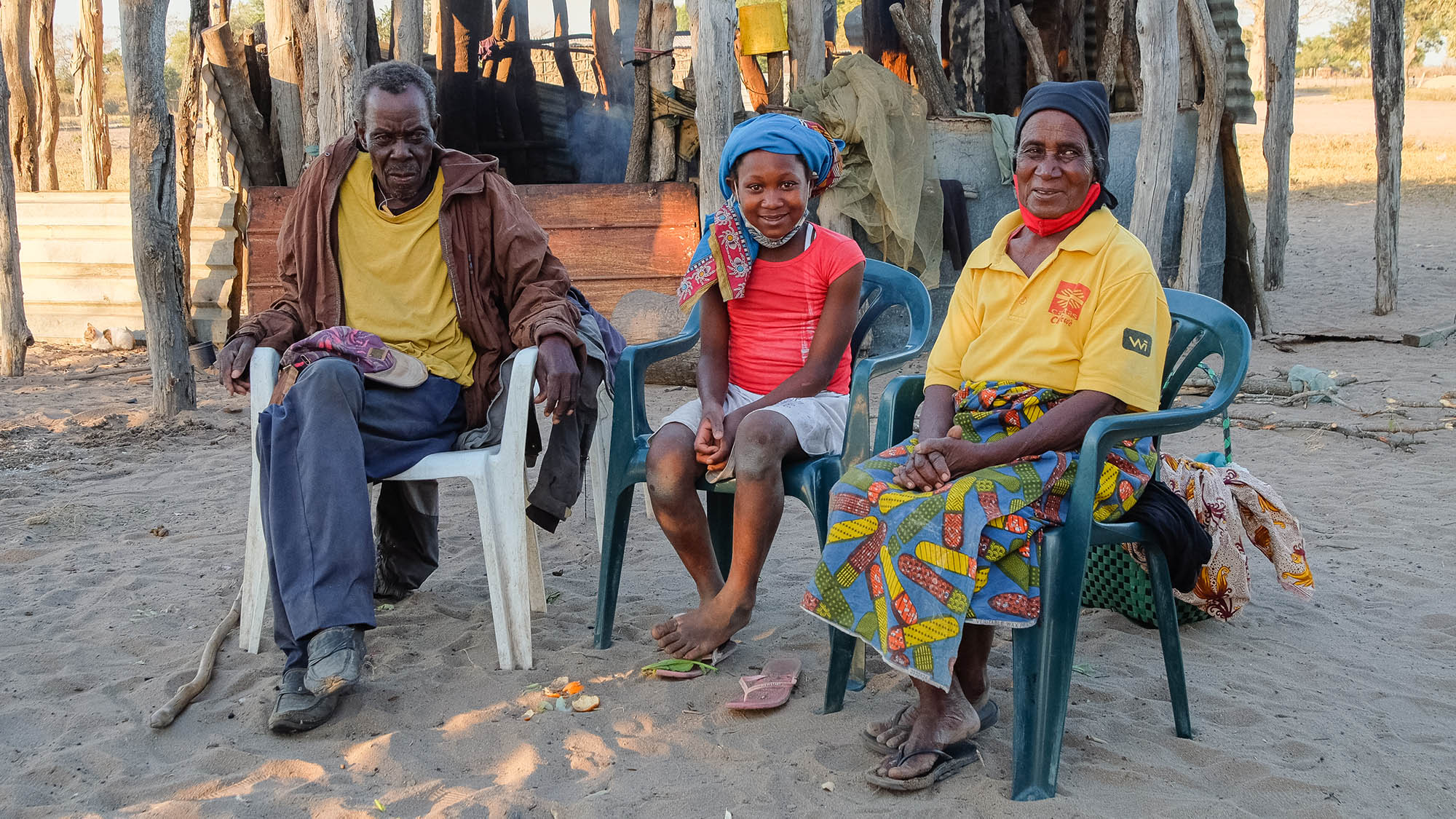 Anatercia sits with her grandfather and grandmother outside their home in Mozambique